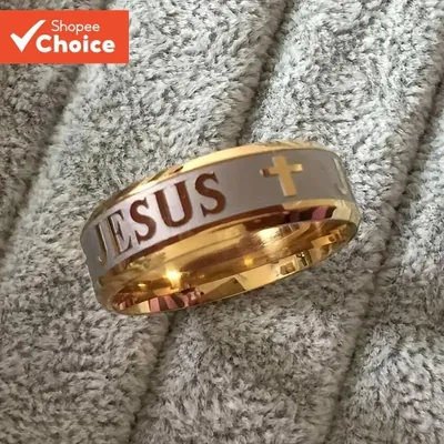 Anel largo dourado com faixa central prateada gravada com a palavra JESUS e uma cruz, sobre tecido cinza felpudo