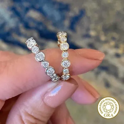 Mão segurando dois anéis de pedras redondas em sequência, um prateado e um dourado, com selo GRA no canto