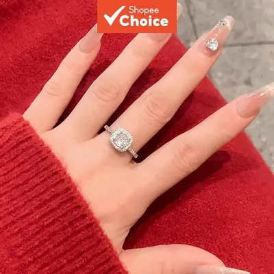 Mão de unhas longas sobre suéter vermelho usando anel prateado com pedra quadrada, halo e aro cravejado