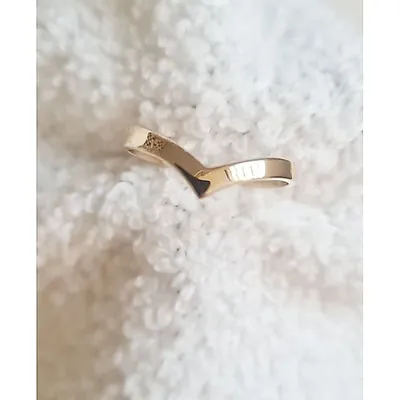 Anel dourado liso em formato de V apoiado sobre tecido branco felpudo