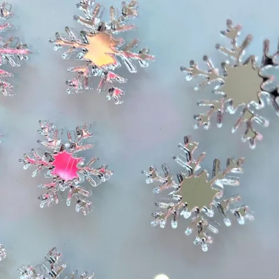 Flocos de neve de acrílico espelhado prateado sobre fundo claro, refletindo tons de rosa e dourado