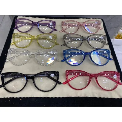 Oito armações de óculos gatinho em cores translúcidas com textura facetada, lentes claras e adesivo de grau, sobre pano bege