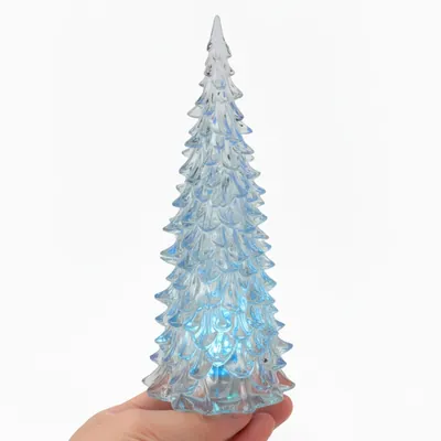 Árvore de Natal de acrílico transparente com galhos em camadas e luz azul na base, apoiada na palma de uma mão
