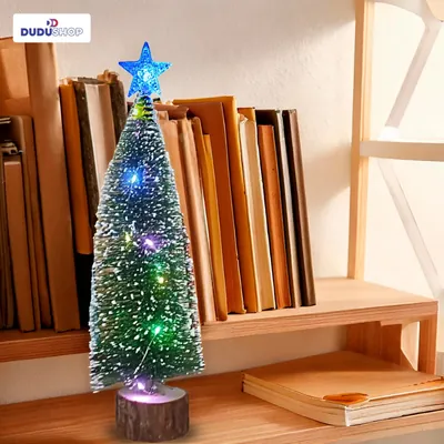 Árvore de Natal fina com pontas brancas, luzes coloridas e estrela azul no topo, sobre estante com livros