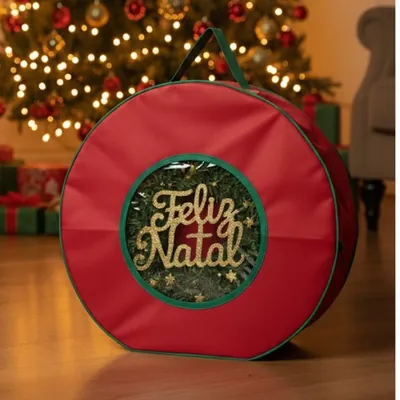 Bolsa redonda vermelha com debrum verde, alça no topo e visor transparente mostrando guirlanda com Feliz Natal dourado