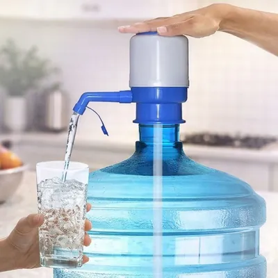 Mão pressionando bomba manual azul e cinza em galão de água, que enche um copo com gelo por um bico curvo