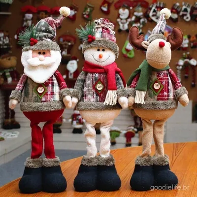 Três bonecos de Natal em pé, Papai Noel, boneco de neve e alce, com casaco xadrez, cachecol e botas pretas, sobre mesa