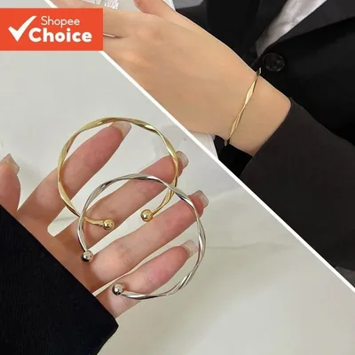 Braceletes abertos torcidos, um dourado e um prateado, com bolinhas nas pontas, e um deles num pulso de blazer