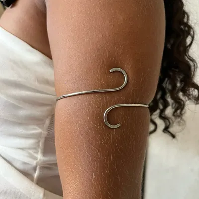 Bracelete prateado de fio liso com pontas curvadas em gancho, usado na parte de cima do braço de uma mulher