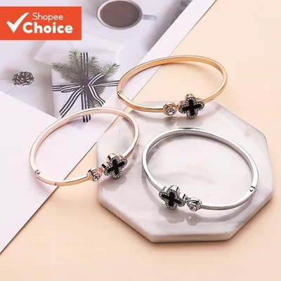 Três braceletes finos nas cores rosé, dourada e prateada, cada um com trevo preto contornado por pedrinhas, sobre mármore