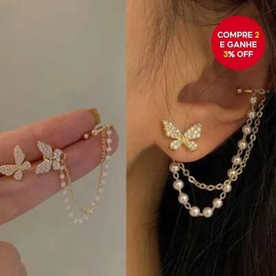Brinco de borboleta dourada cravejada no lóbulo, ligado por corrente dourada e corrente de pérolas a um ear cuff na orelha