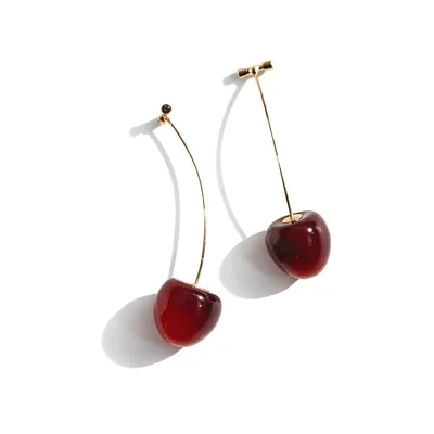 Par de brincos com cereja vermelha translúcida presa a uma haste dourada longa e fina, sobre fundo branco