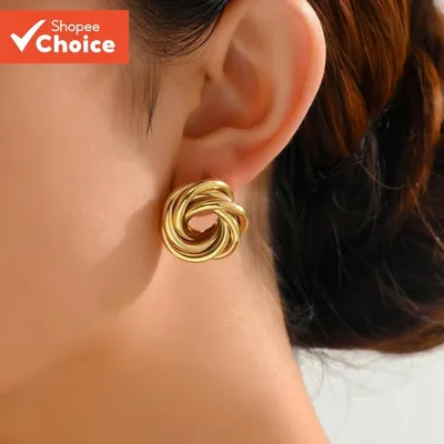 Brinco dourado de fios tubulares entrelaçados em forma de nó, usado na orelha de uma mulher de cabelo castanho preso