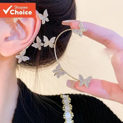 Brinco ear cuff dourado com borboletas de pedrinhas brilhantes contornando a orelha; outra peça na mão