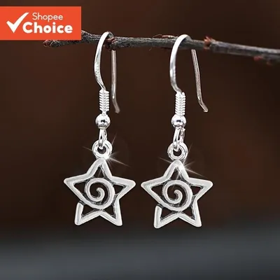 Par de brincos pendentes em forma de estrela vazada com espiral no meio, pendurados num galho seco sobre fundo marrom
