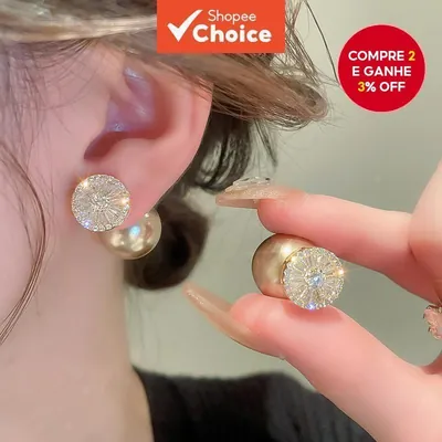 Brinco com disco dourado cravejado de zircônias na frente do lóbulo e pérola grande atrás, usado na orelha e segurado na mão