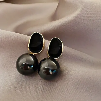 Par de brincos com placa oval de esmalte preto e borda dourada e grande pérola preta, sobre tecido acetinado rosado