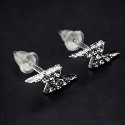 Par de brincos prateados em forma de raio cravejados de pedrinhas, com tarrachas transparentes, sobre fundo preto