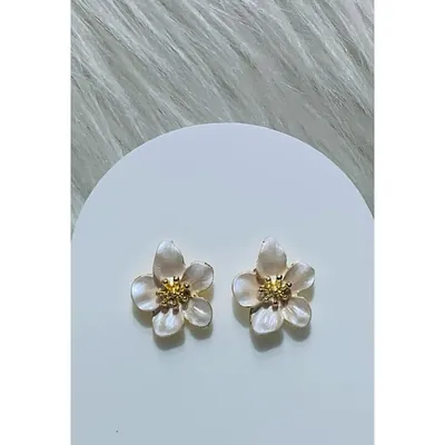 Par de brincos em forma de flor de cinco pétalas brancas peroladas com miolo dourado sobre cartão branco e pelo sintético