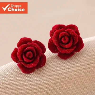Par de brincos em forma de rosa vermelha escura com textura aveludada, apoiados sobre tecido bege