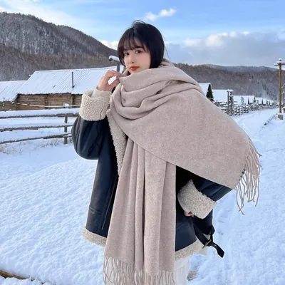 Mulher na neve com cachecol largo cor aveia com franjas enrolado no pescoço e jaqueta preta forrada