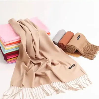 Pashmina bege com franjas aberta sobre mesa, ao lado de pilha de pashminas coloridas e outras enroladas