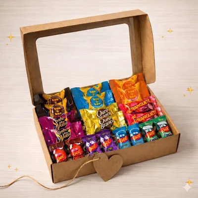 Caixa de papelão kraft aberta com tampa de visor, cheia de bombons e chocolates embalados e tag de coração com barbante