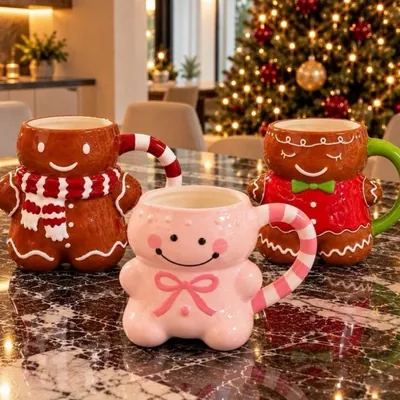 Três canecas de cerâmica em formato de boneco de gengibre, marrons e rosa, sobre bancada de mármore com árvore ao fundo