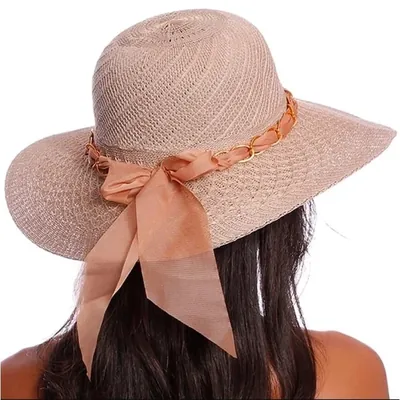 Mulher de costas usando chapéu de aba larga em trama rosé com faixa de tecido, laço comprido e elos dourados