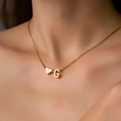 Colar dourado de corrente fina com um coração e a letra G, usado rente à base do pescoço