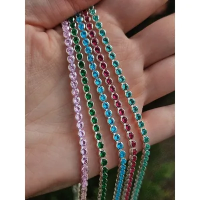 Mão segurando cinco rivieras de zircônias redondas nas cores rosa, verde, azul, pink e verde-água