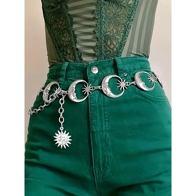 Cinto de corrente prateado com luas e estrelas e pingente de sol sobre calça jeans verde de cintura alta