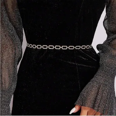 Cinto de corrente prateada com elos ovais de strass sobre vestido preto de veludo com mangas transparentes