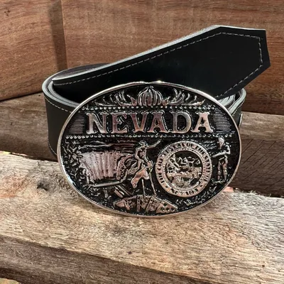 Cinto preto com pesponto claro e fivela oval prateada escrita Nevada, com peão, carroça e selo, sobre tábuas de madeira