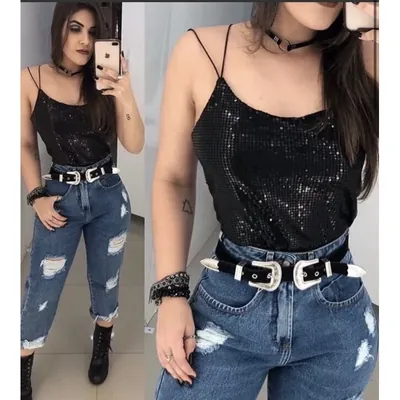 Mulher de regata de paetê preta e calça jeans rasgada usando cinto preto com duas fivelas prateadas