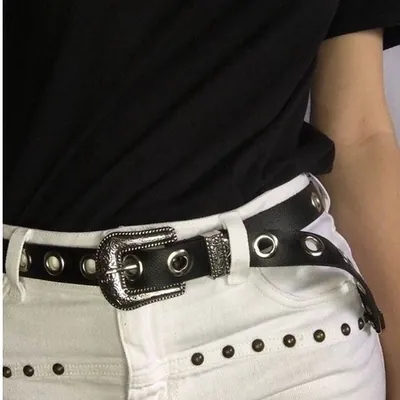 Cinto preto com ilhós prateados e fivela trabalhada usado com camiseta preta e calça branca com tachas