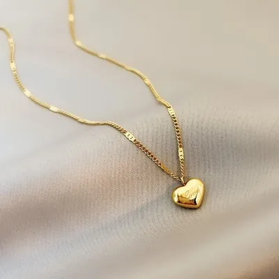 Colar dourado de corrente fina com pingente de coração abaulado gravado com a palavra Love, sobre tecido cinza acetinado