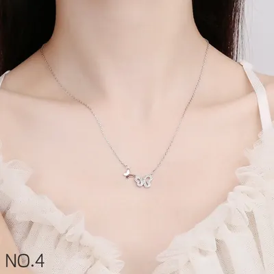 Colar prateado com uma borboleta lisa e outra vazada com pedrinhas, usado com blusa branca de tule