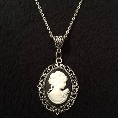 Pingente oval de camafeu com perfil feminino branco em fundo preto, moldura prateada rendada e corrente fina
