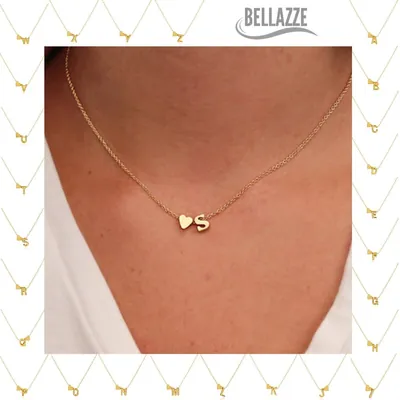 Colar dourado curto com um pequeno coração e a letra S lado a lado, usado com blusa branca de decote V