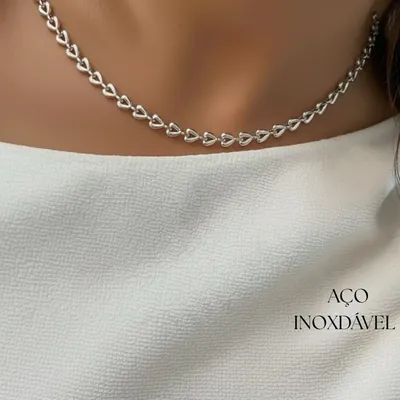 Colar curto de elos em forma de coração prateados no pescoço de mulher com blusa branca