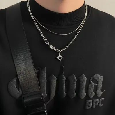 Colar prateado de corrente grossa com estrela pontuda e elos com strass, sobre moletom preto, junto a uma corrente fina