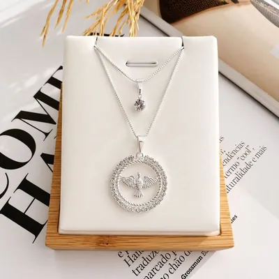 Colar prateado de duas correntes, uma com ponto de luz e outra com medalha de pomba do Espírito Santo, em expositor branco