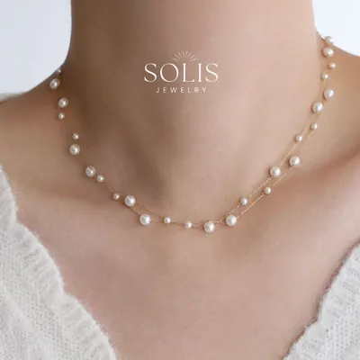 Pescoço feminino com colar de duas correntes douradas finas e pérolas brancas de tamanhos variados, sobre suéter branco