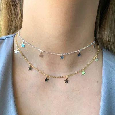 Pescoço com dois colares curtos de corrente fina, um prateado e um dourado, com várias estrelinhas penduradas