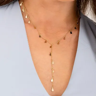 Colar dourado em Y com pequenas gotas penduradas, usado sobre blusa azul-clara de decote V