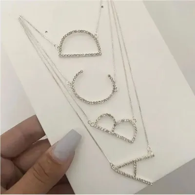 Quatro colares prateados com as letras A, B, C e D vazadas e cravejadas, presos em cartela branca