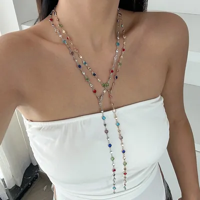 Mulher de top branco tomara que caia usando colar longo de pedrinhas coloridas, com as pontas caindo pela frente