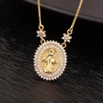 Medalha oval dourada com Virgem Maria em relevo, moldura de pedrinhas brancas e corrente veneziana sobre madeira escura