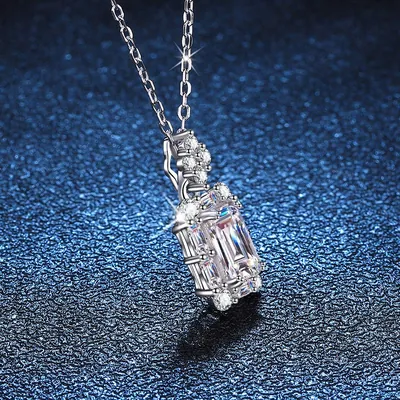 Pingente com pedra retangular transparente cercada de pedrinhas, em corrente fina prateada sobre fundo azul brilhante